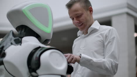 Ein-Mann-Im-Hemd-Kommuniziert-Mit-Einem-Weißen-Roboter,-Stellt-Fragen-Und-Drückt-Mit-Den-Fingern-Auf-Den-Bildschirm